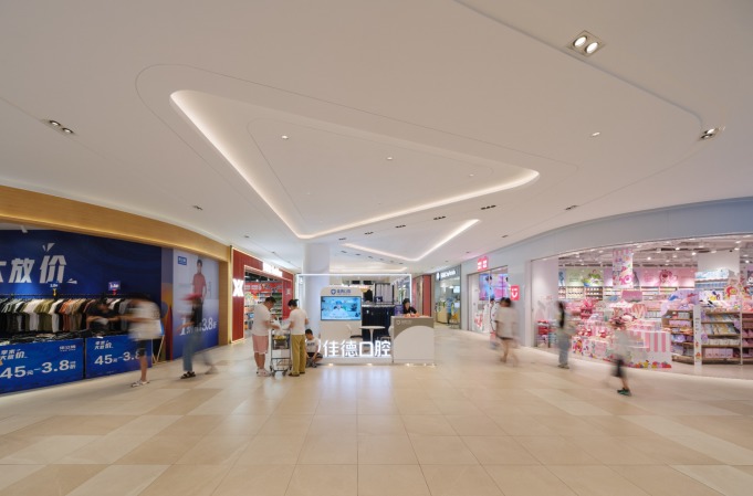 现代购物中心内，人们在明亮的走廊中行走，天花板装饰有圆环形灯光，商店包括Calvin Jeans和DISSONA。