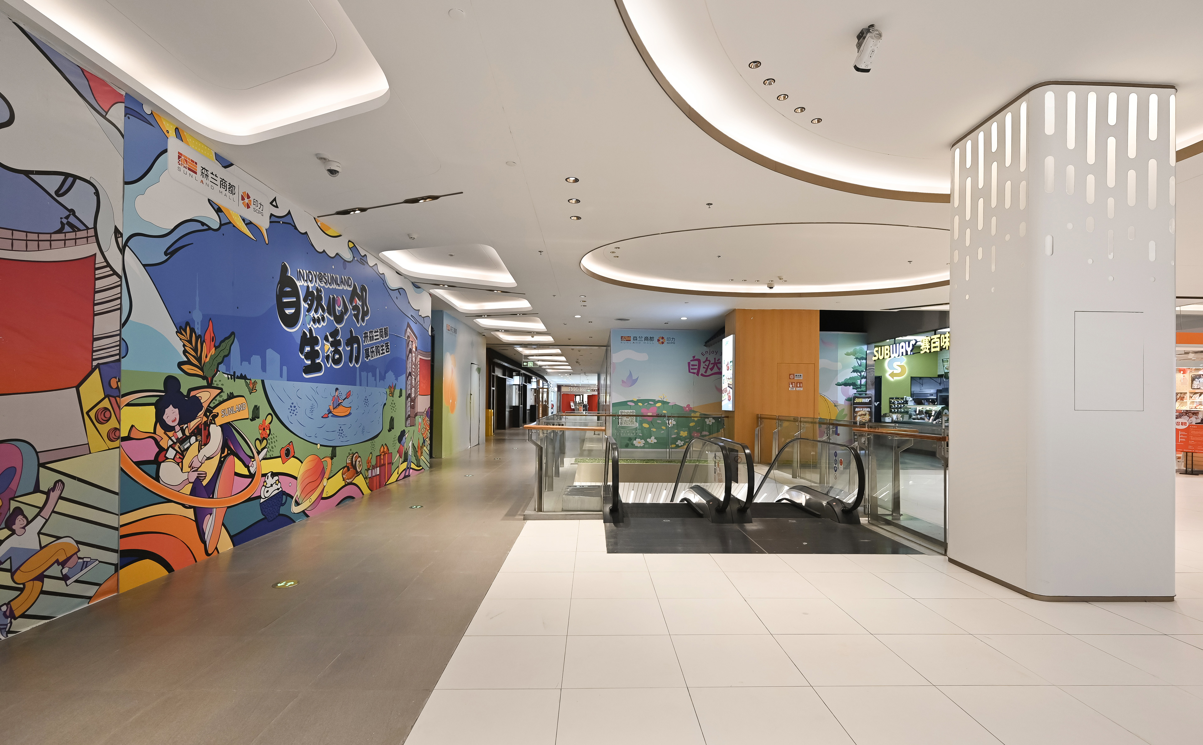 现代购物中心内，人们在明亮的走廊中行走，天花板装饰有圆环形灯光，商店包括Calvin Jeans和DISSONA。