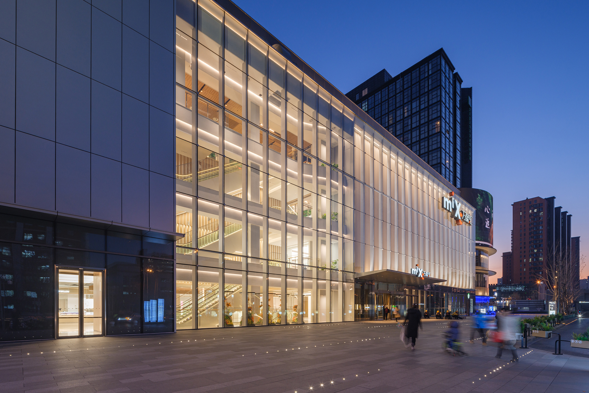 现代购物中心内，人们在明亮的走廊中行走，天花板装饰有圆环形灯光，商店包括Calvin Jeans和DISSONA。