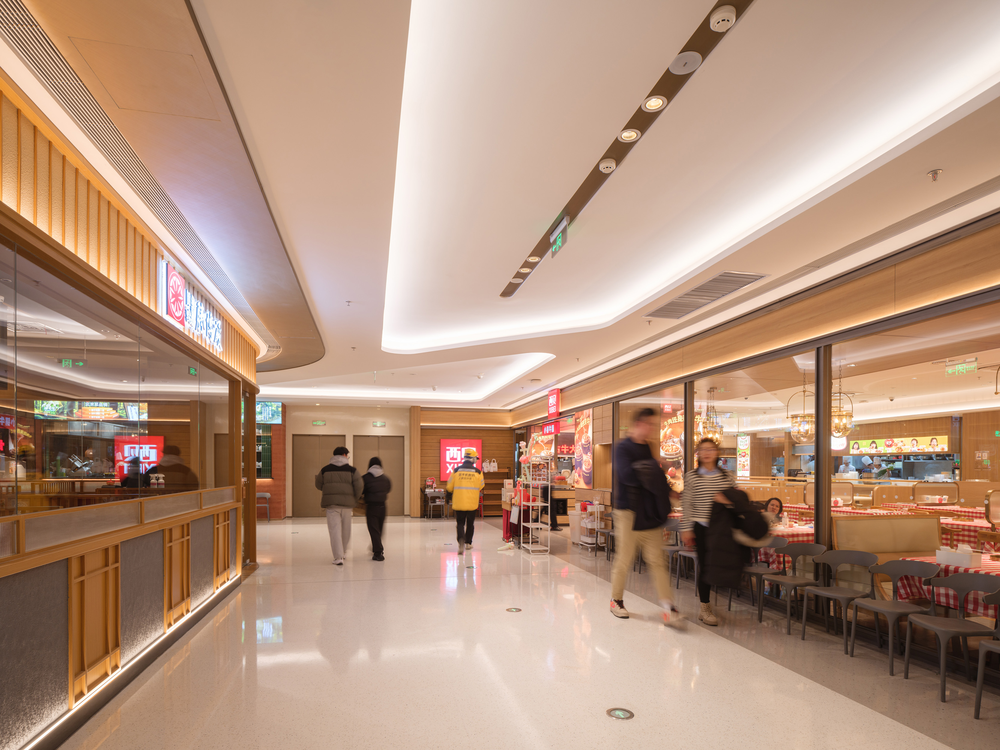 购物中心内现代圆形天花板，中央区域有三角形镜面装饰，周围环绕暖色灯光。