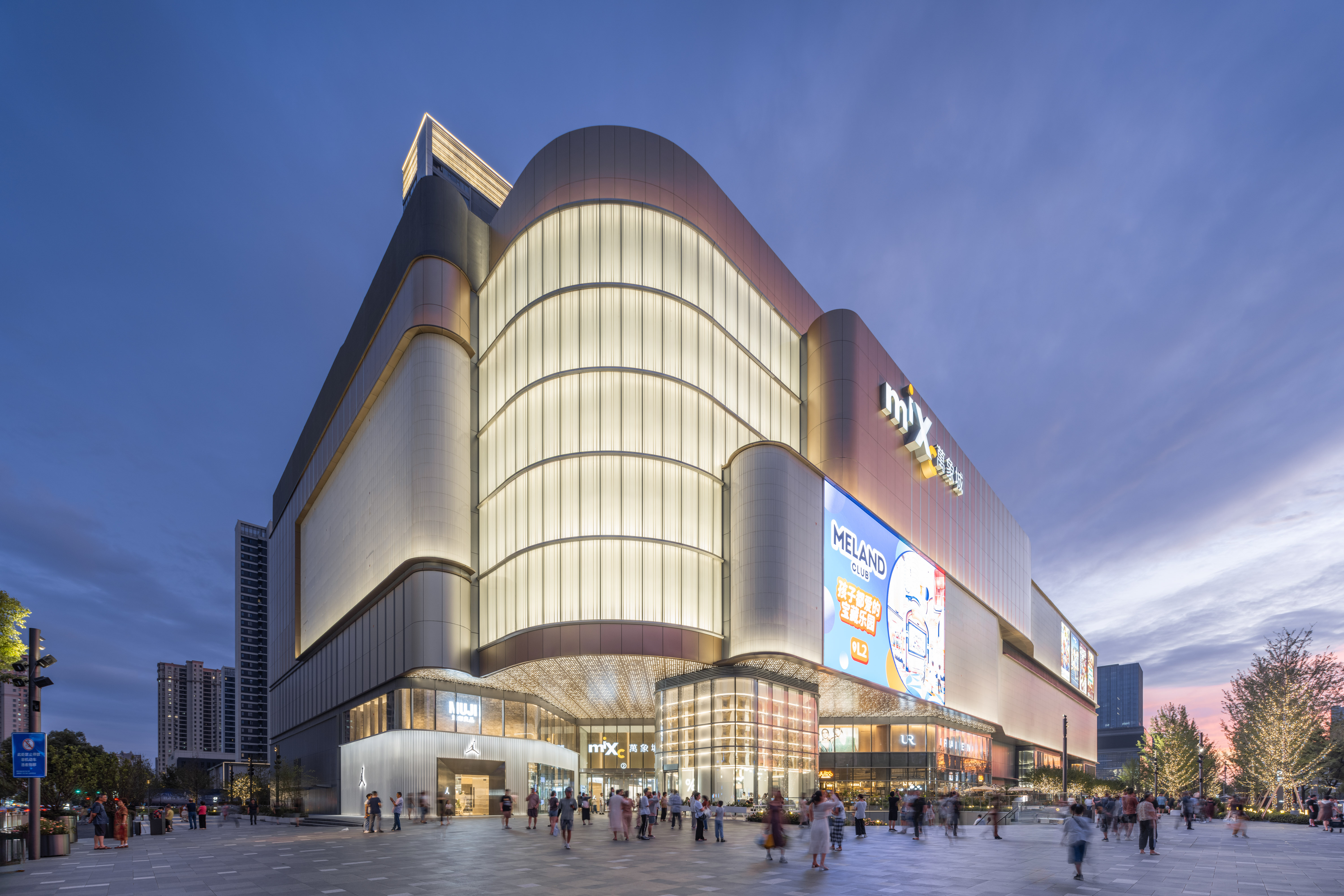 购物中心内现代圆形天花板，中央区域有三角形镜面装饰，周围环绕暖色灯光。