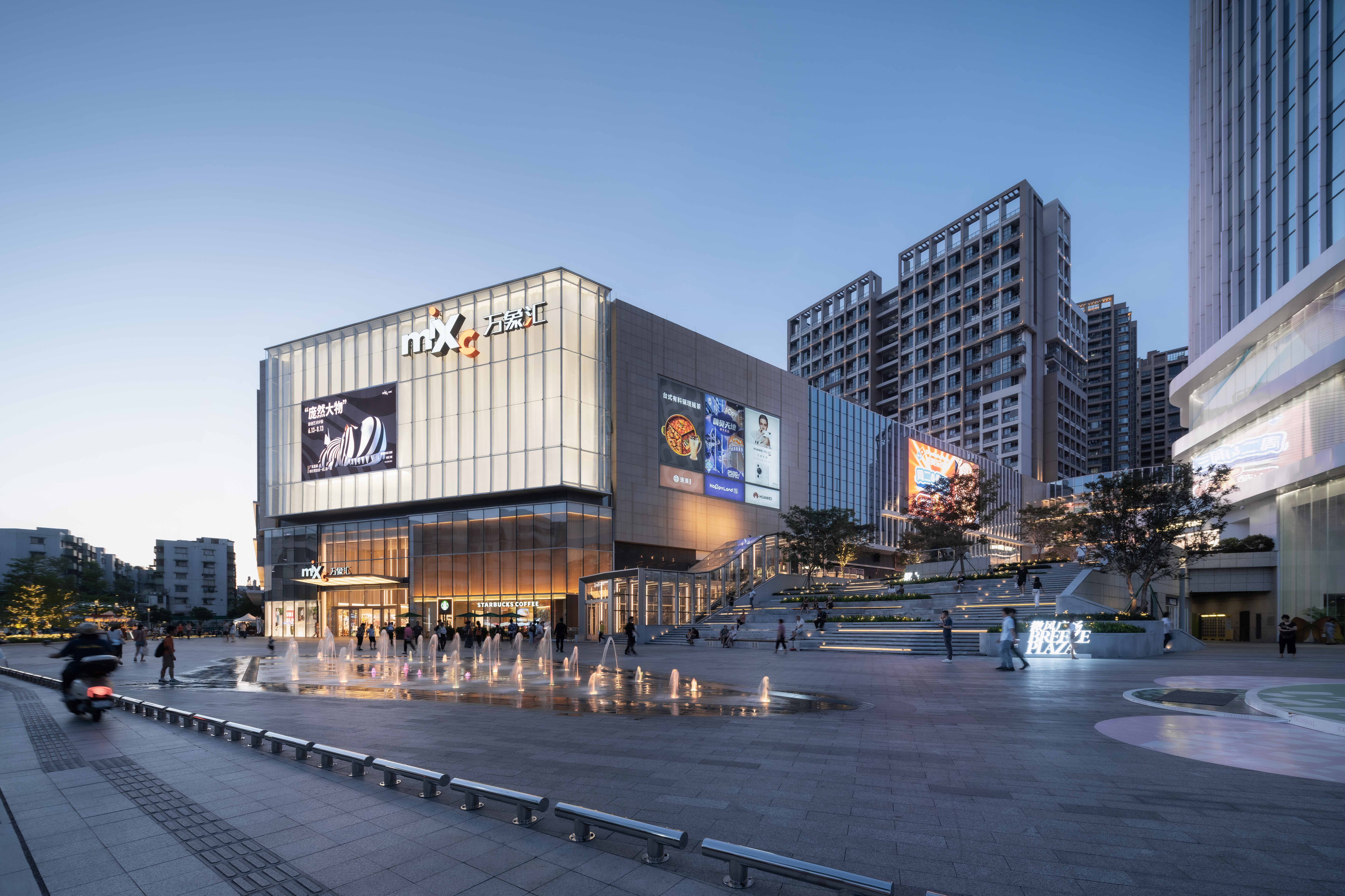 购物中心内现代圆形天花板，中央区域有三角形镜面装饰，周围环绕暖色灯光。