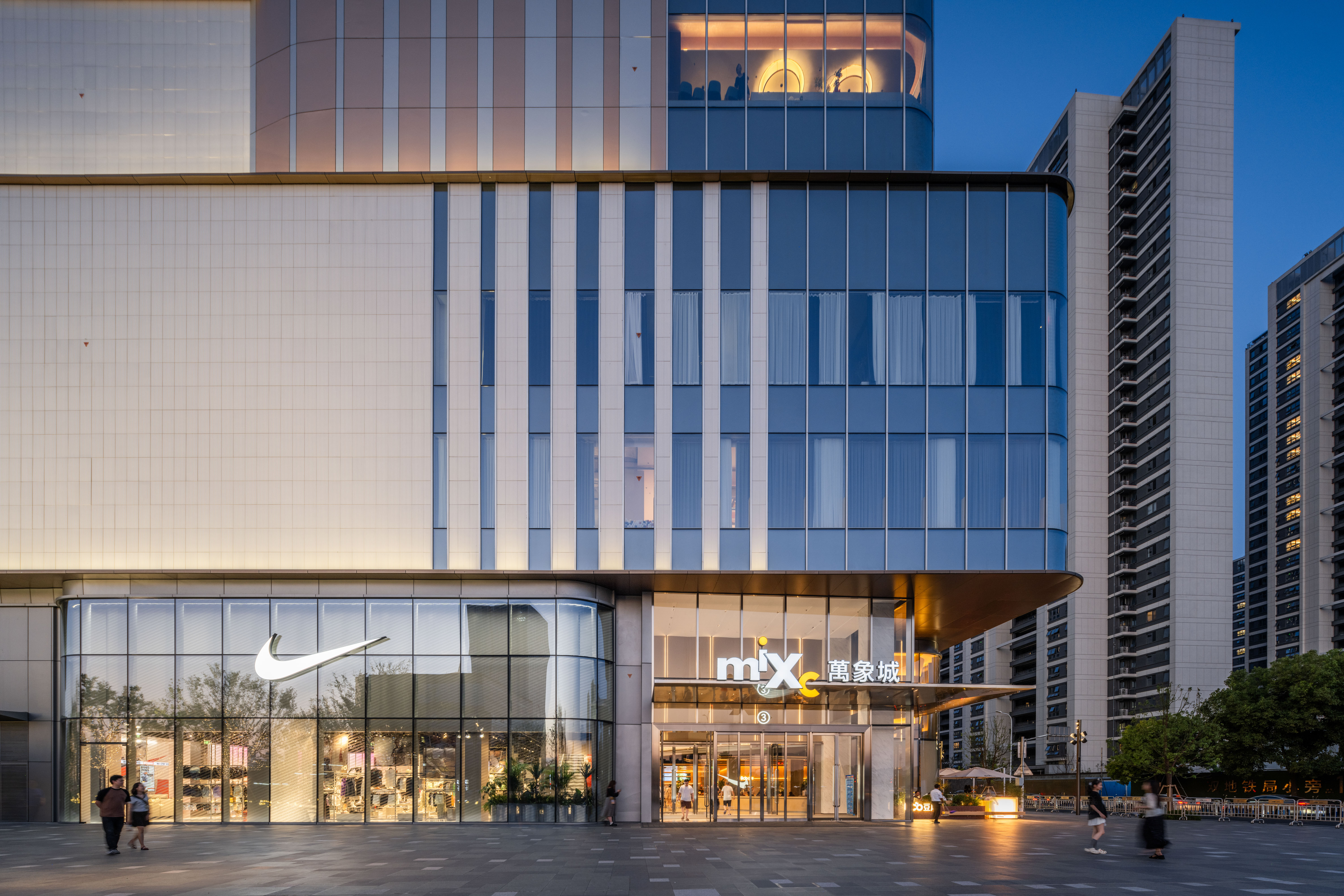 购物中心内现代圆形天花板，中央区域有三角形镜面装饰，周围环绕暖色灯光。