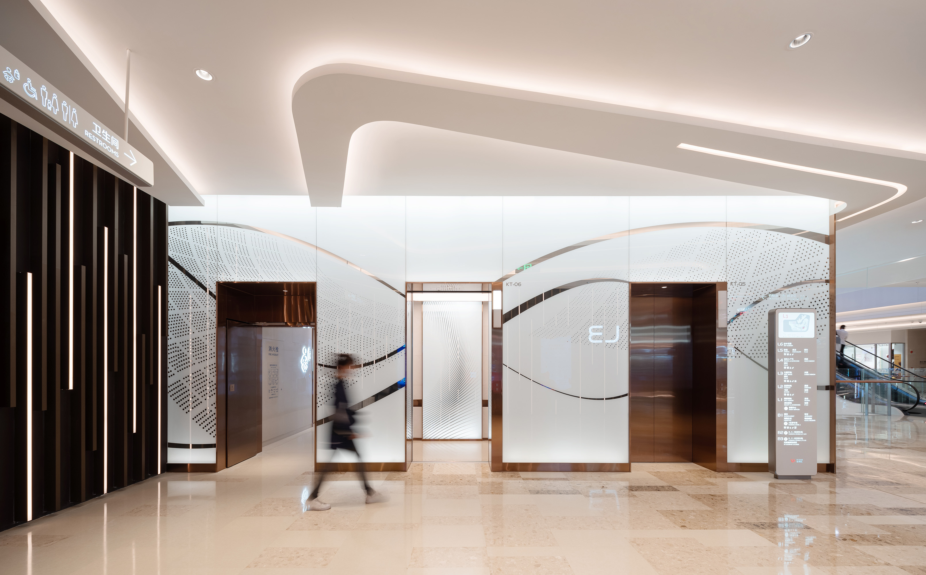 购物中心内现代圆形天花板，中央区域有三角形镜面装饰，周围环绕暖色灯光。