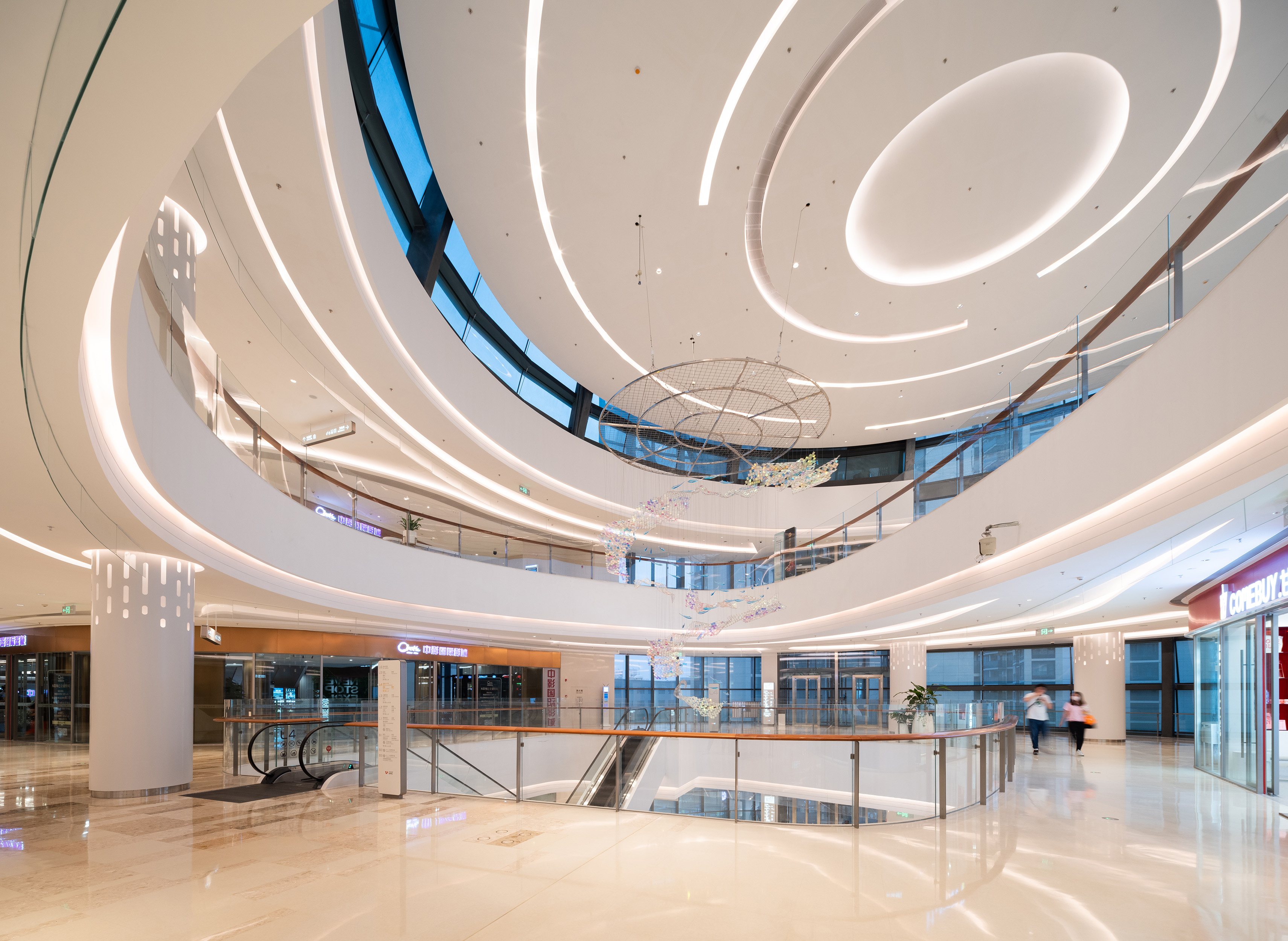 现代购物中心内，人们在明亮的走廊中行走，天花板装饰有圆环形灯光，商店包括Calvin Jeans和DISSONA。