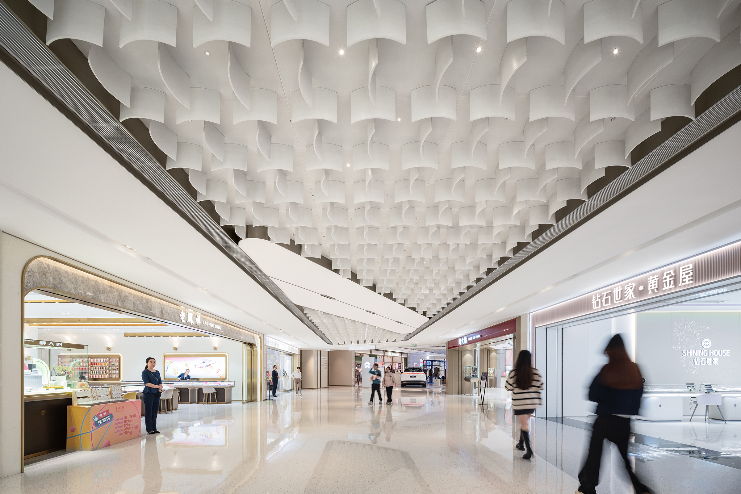 现代购物中心内，人们在明亮的走廊中行走，天花板装饰有圆环形灯光，商店包括Calvin Jeans和DISSONA。