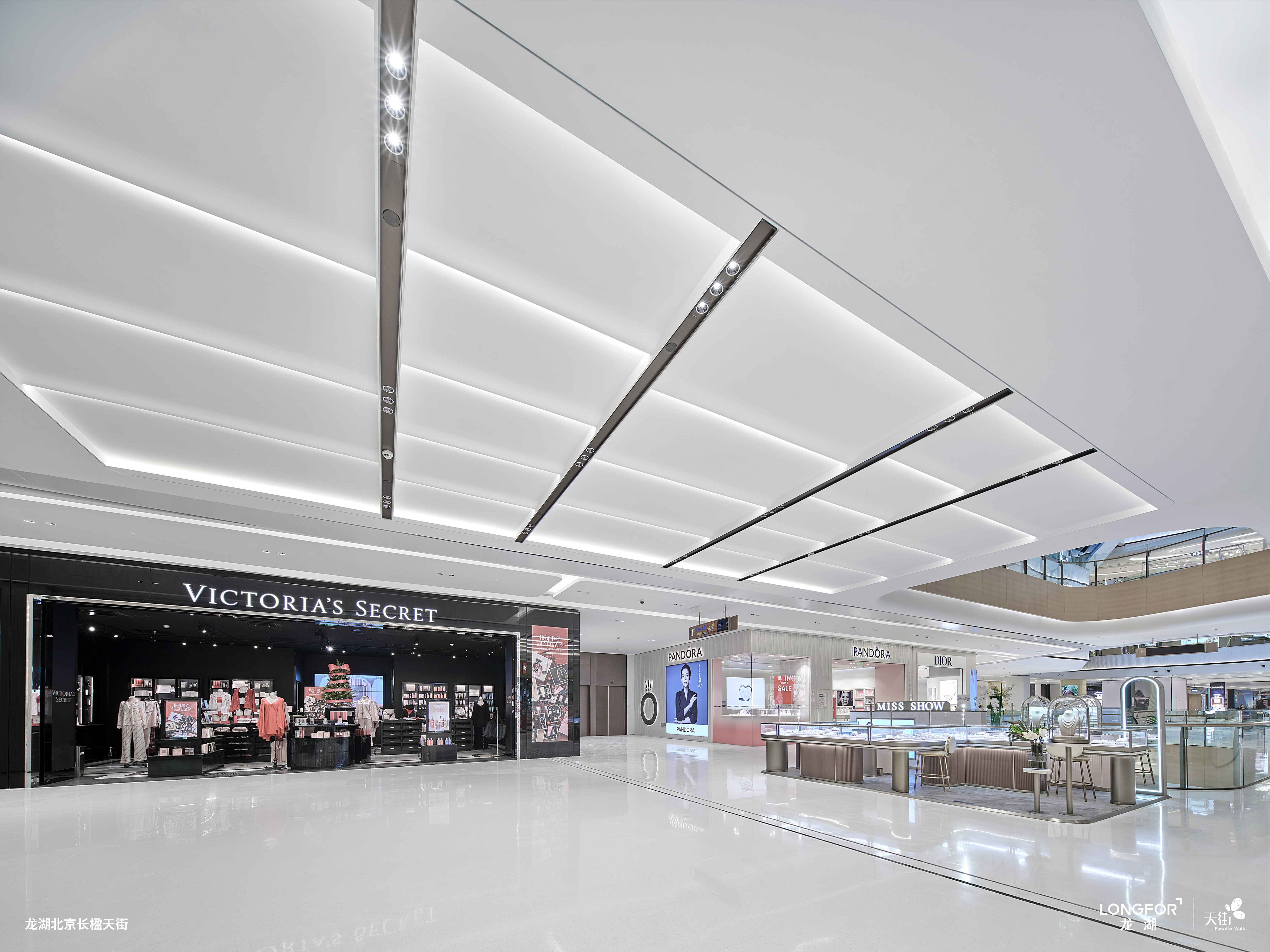 购物中心内现代圆形天花板，中央区域有三角形镜面装饰，周围环绕暖色灯光。