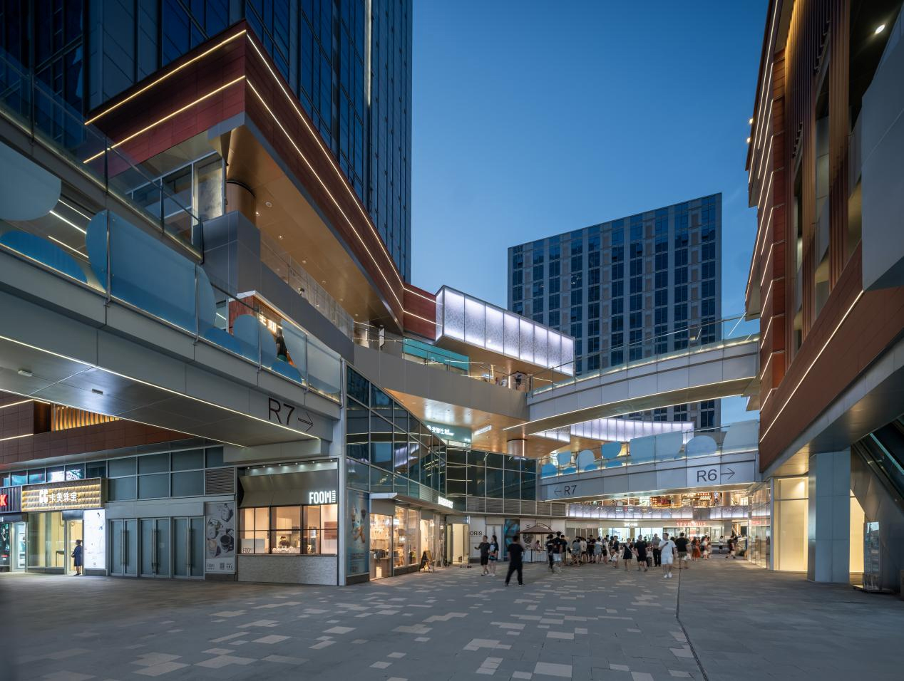 现代购物中心内部，中央有大型玻璃穹顶和多层环绕商铺，右侧有自动扶梯。