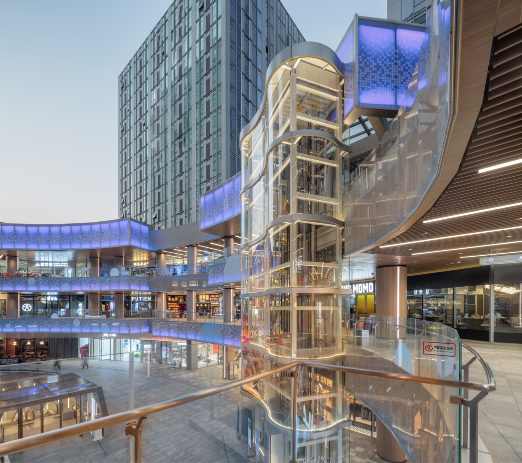 购物中心内现代圆形天花板，中央区域有三角形镜面装饰，周围环绕暖色灯光。