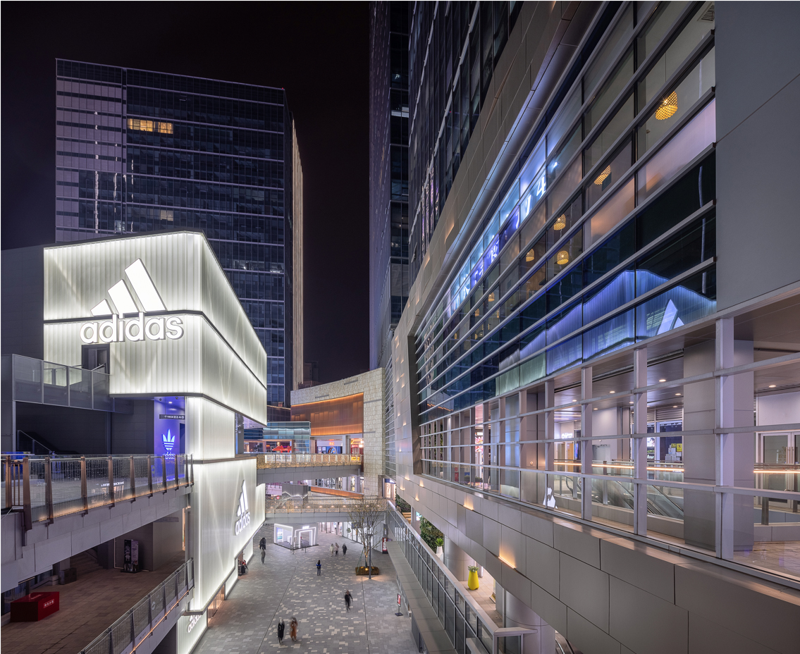 购物中心内现代圆形天花板，中央区域有三角形镜面装饰，周围环绕暖色灯光。